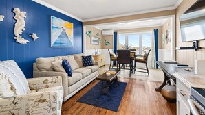 Un salon avec un mur bleu, un canapé blanc, une table basse et un coin repas avec vue.