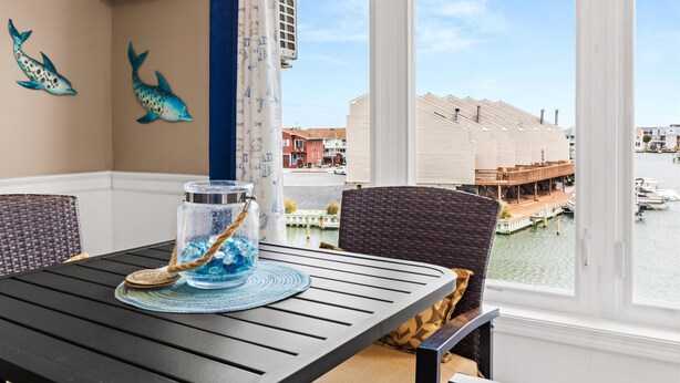 Un coin repas comprenant une table, des chaises, un vase décoratif et une vue sur un canal bordé de bâtiments et de bateaux.