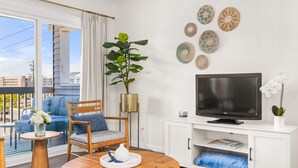 Ett modernt vardagsrum med en stor tv-skärm, ett soffbord i trä, en blå soffa och en krukväxt.