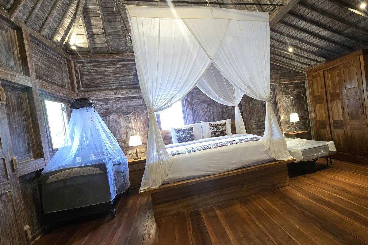 Una habitación rústica de madera con una cama grande, una mesita de noche, un armario y una ventana con cortinas.