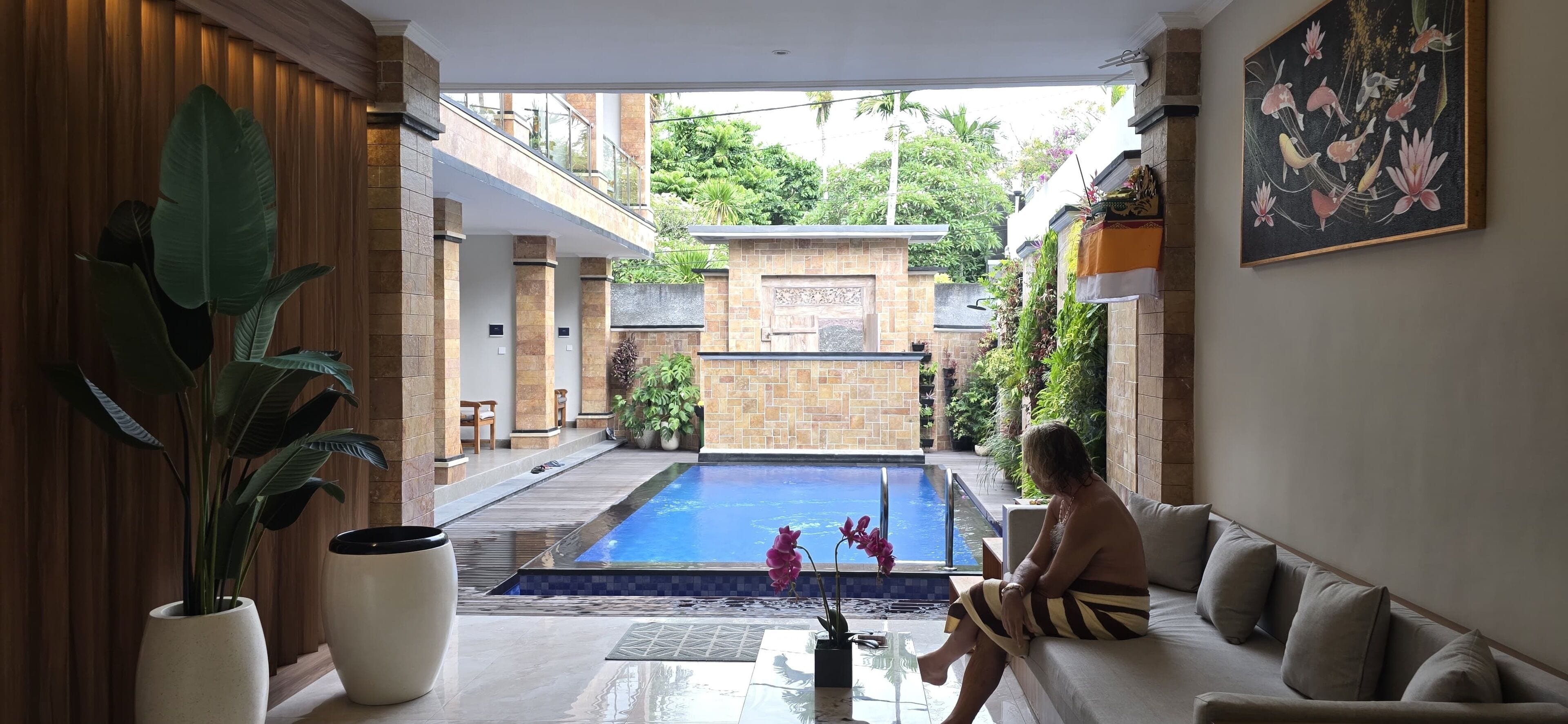 Un área interior de piscina moderna con un separador de vidrio, una zona de estar con sofá y una planta grande en maceta.