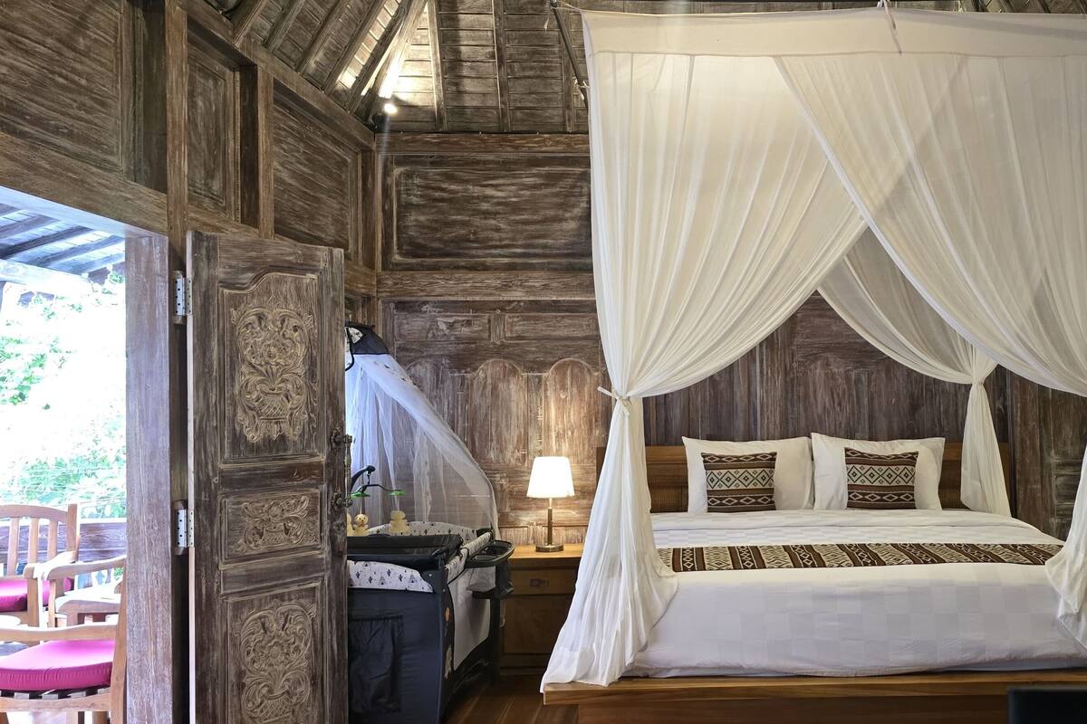 Une pièce en bois avec un lit sous un dais, deux tables de chevet avec des lampes et une chaise.