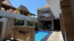 A modern building with a swimming pool, a sign reading "Plaza", and traditional architecture in the background. - Mara Inn (Nusa Dua)