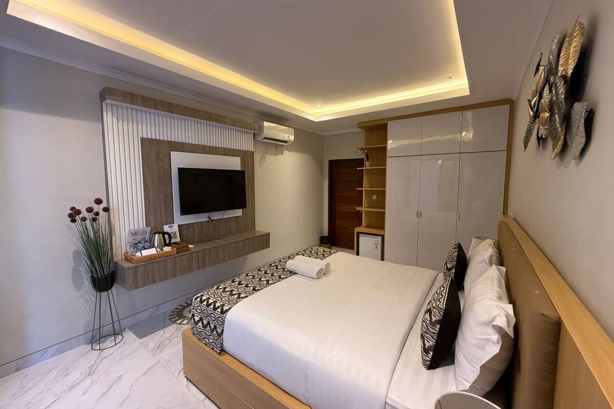 Une chambre d’hôtel moderne équipée d’un lit, d’une télévision, d’une armoire et d’un petit bureau agrémenté d’une plante.