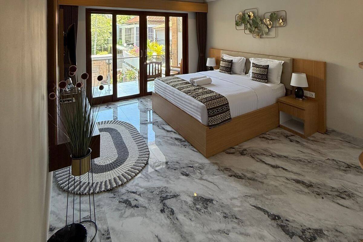 Une chambre spacieuse avec un grand lit, une table de chevet, une plante en pot et une vue sur l’extérieur grâce à une porte-fenêtre coulissante.