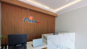 A reception desk with a wooden backdrop, a laptop, a printer, and a sign that reads "Mara". - Mara Inn (Nusa Dua)