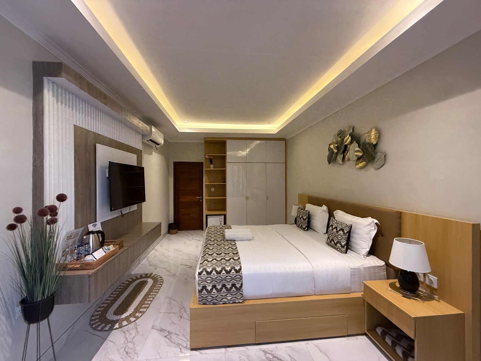 A modern bedroom with a large bed, a TV mounted on the wall, a bedside table with a lamp, and a built-in wardrobe.