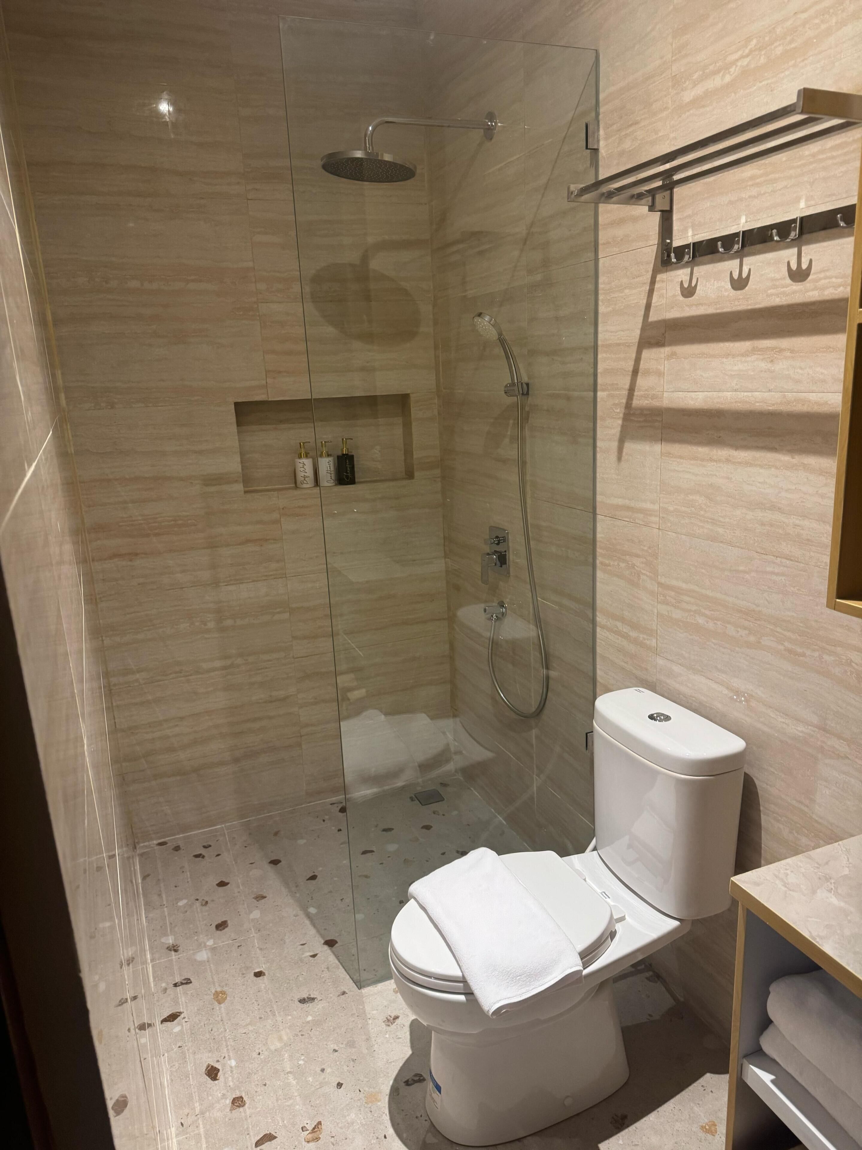 Un baño moderno con ducha de vidrio, inodoro y tocador con barra para toallas.