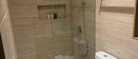 Un baño moderno con ducha de vidrio, inodoro y tocador con barra para toallas.