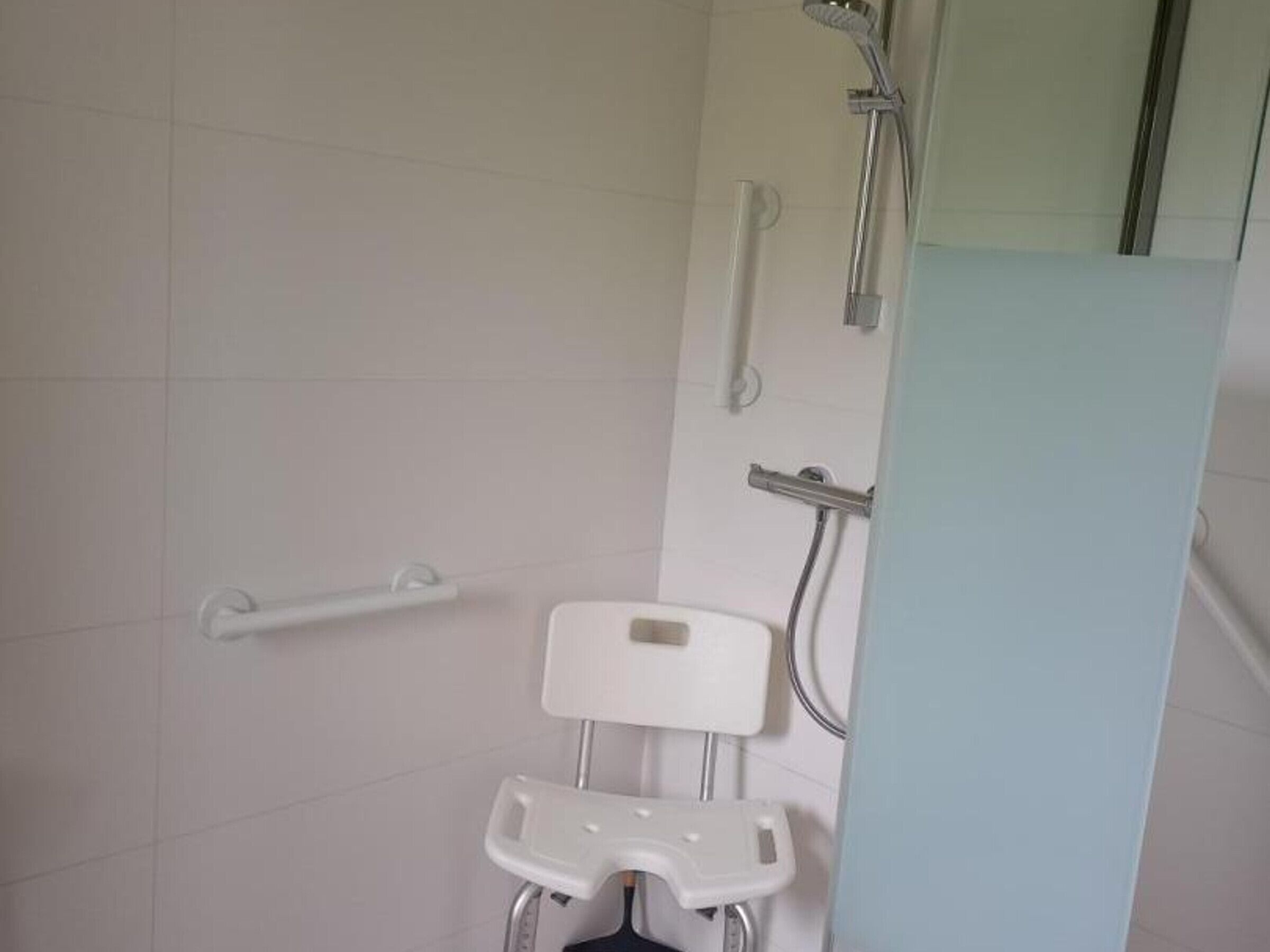 Een badkamer met douche, toilet en een greep.