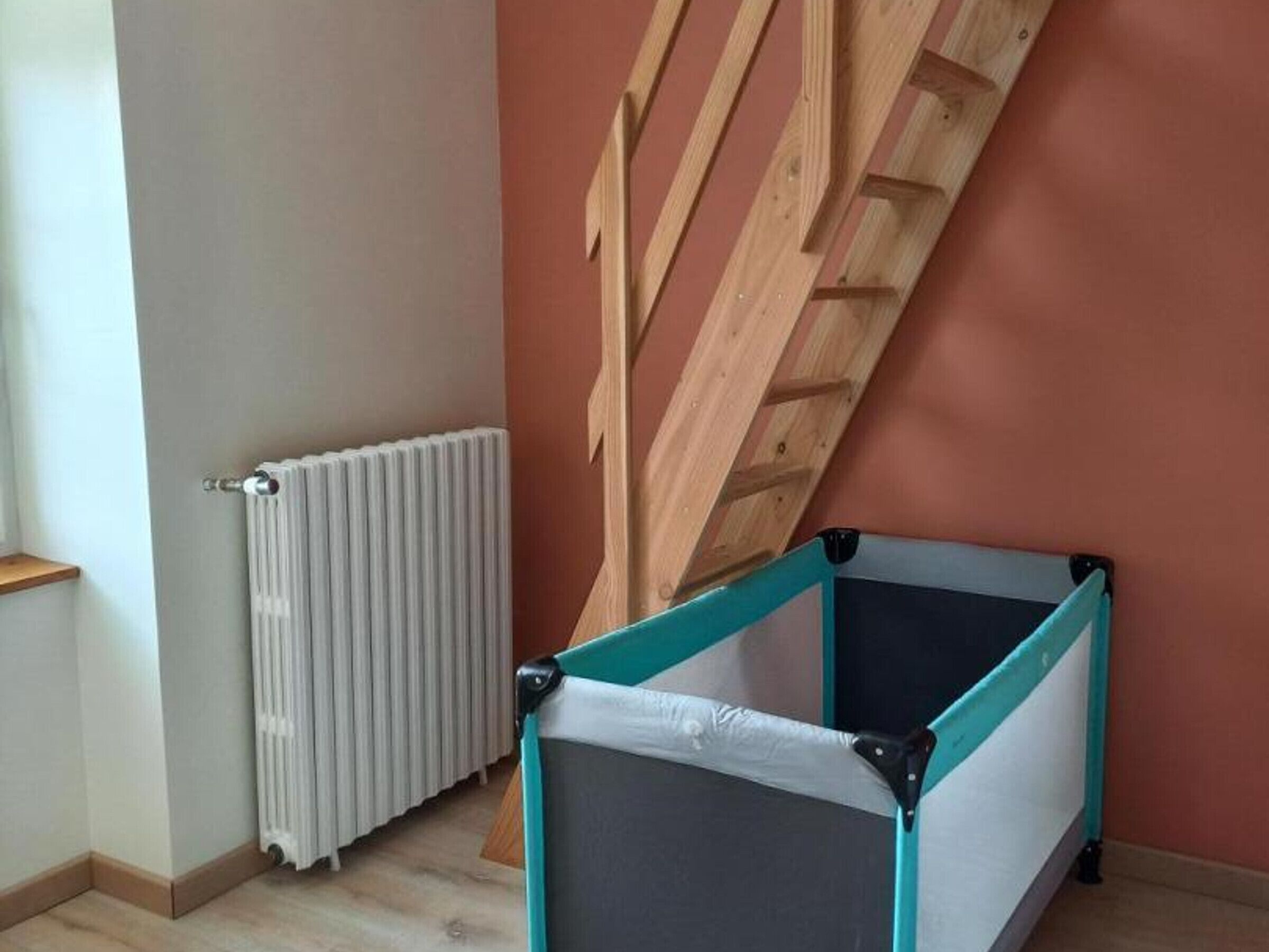 Ein Zimmer mit einem weißen Heizkörper, einer schrägen Holzbalkendecke und einem Spielbereich in Türkis und Weiß.