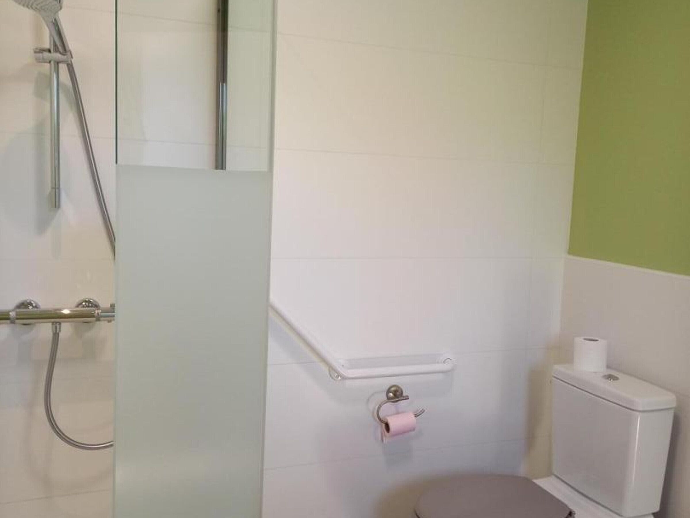 A bathroom with a shower, toilet, and a small shelf with a toilet paper holder.