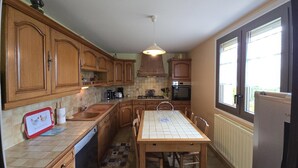 A kitchen with wooden cabinets, a tiled backsplash, a dining table with chairs, and a window with blinds.