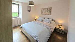 A bedroom with a large bed, two bedside tables with lamps, a world map on the wall, and a window with a view of greenery.