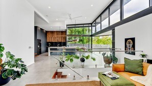 A modern kitchen with a central island, a dining area with a glass railing, and a living room with a sofa and a coffee table. - Belle Escapes Bluewater Breeze (Trinity Beach)