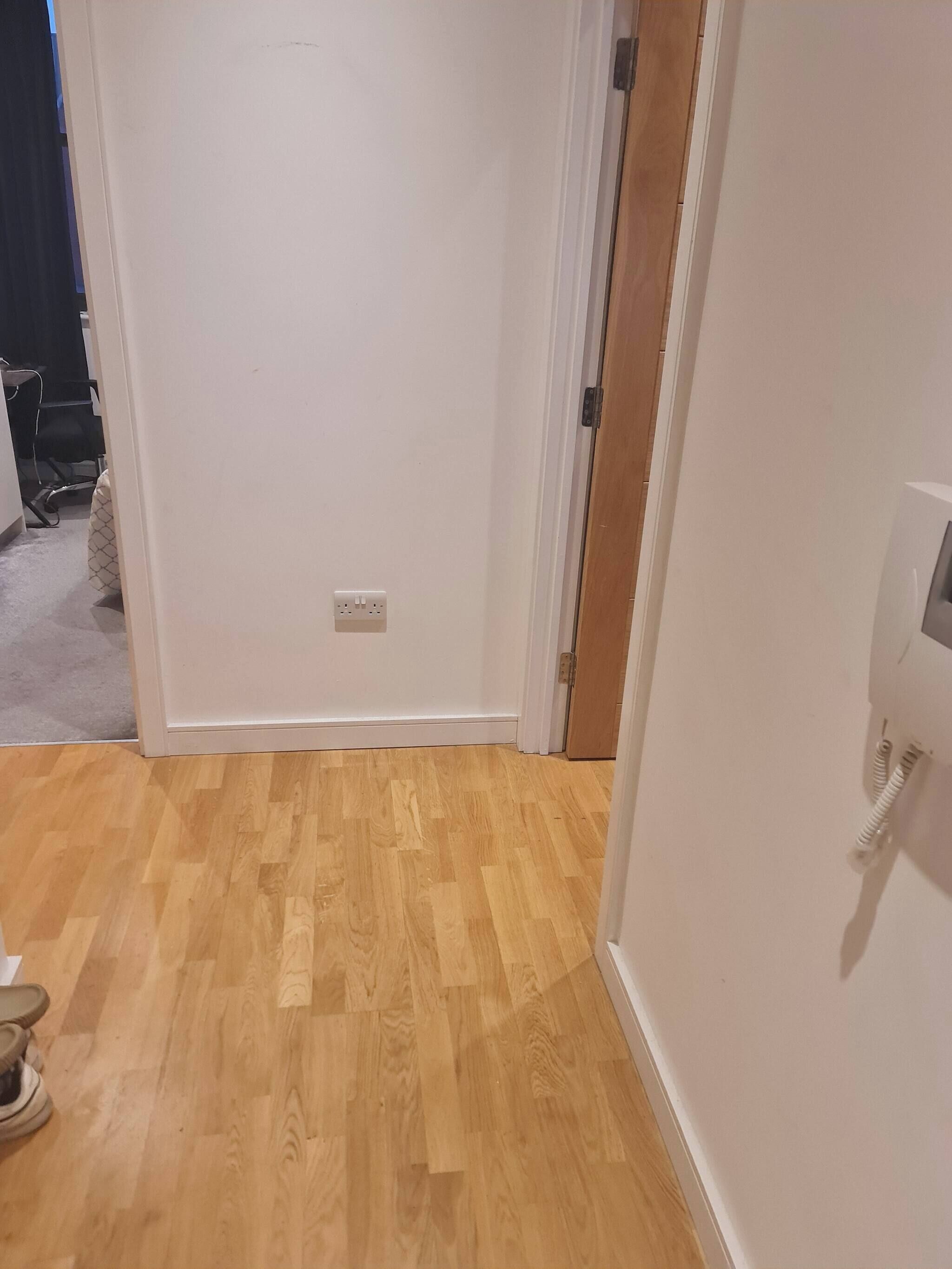 Una habitación con piso de madera, paredes blancas y una puerta que da a otra estancia.
