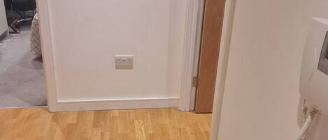 Una habitación con piso de madera, paredes blancas y una puerta que da a otra estancia.