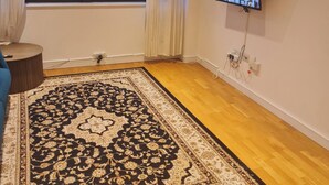 A living room with a large window, a flat-screen TV mounted on the wall, a patterned rug, and a wooden floor. - 2 Beds Flat Centrally Located 2 Mins From Station (Romford)