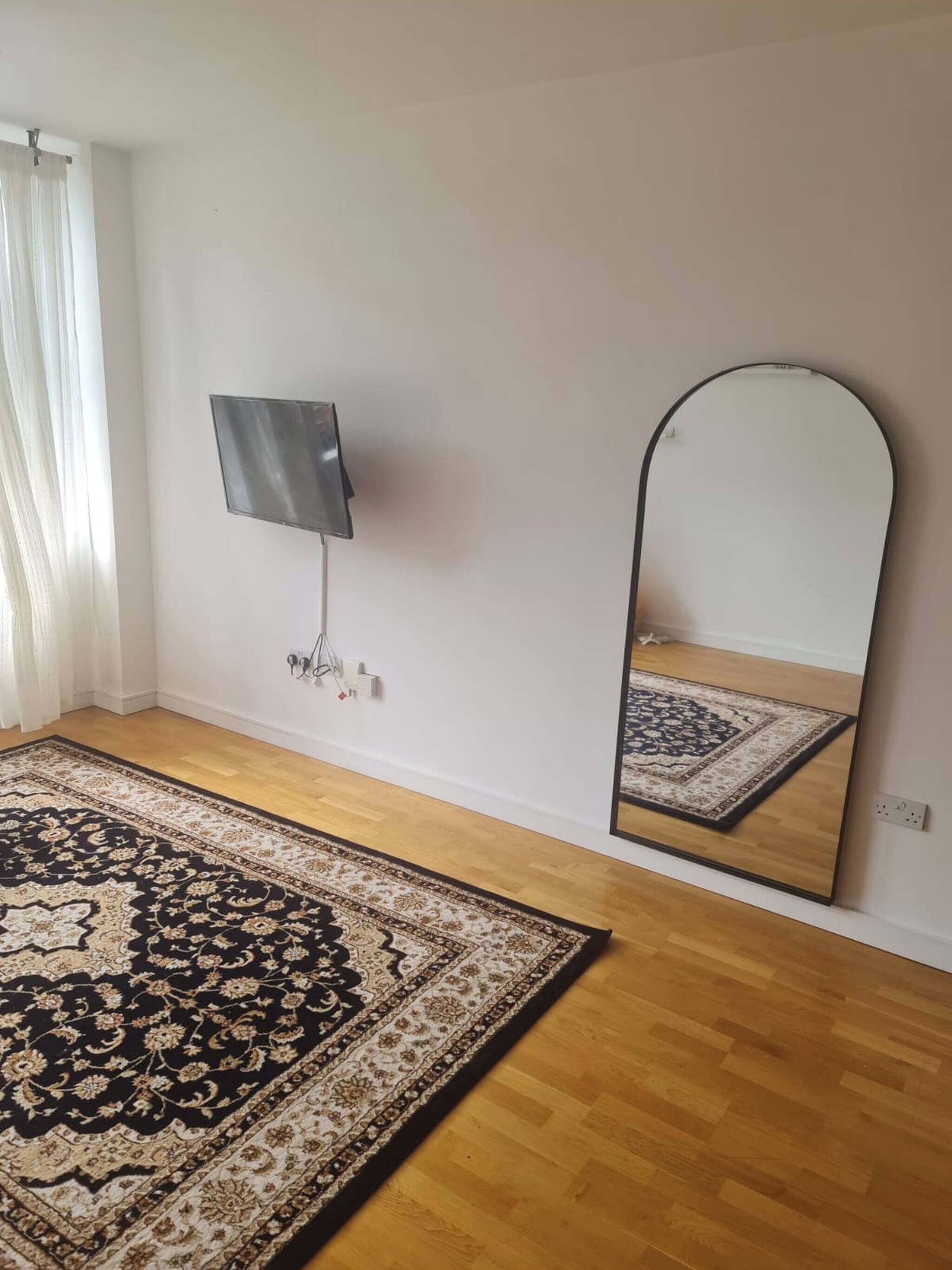 A room with a large mirror, a flat-screen TV, and a patterned rug on a wooden floor.