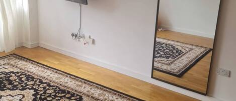 A room with a large mirror, a flat-screen TV, and a patterned rug on a wooden floor.