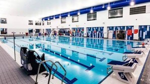 A large indoor swimming pool with multiple lanes, lifeguard chairs, and a poolside area with a tiled walkway. - 2 Beds Flat Centrally Located 2 Mins From Station (Romford)