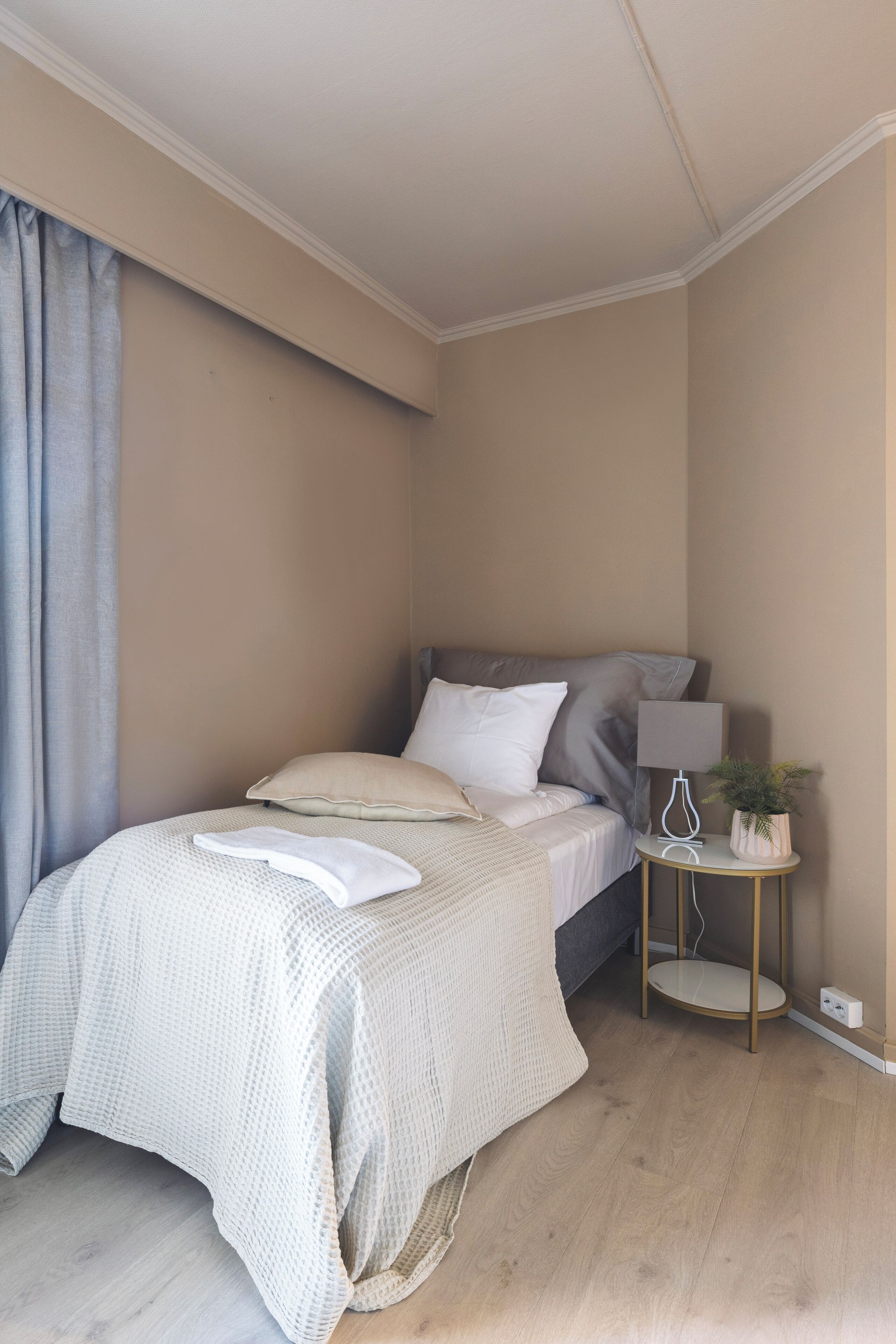 A bedroom with a bed, a bedside table with a lamp, and a potted plant.