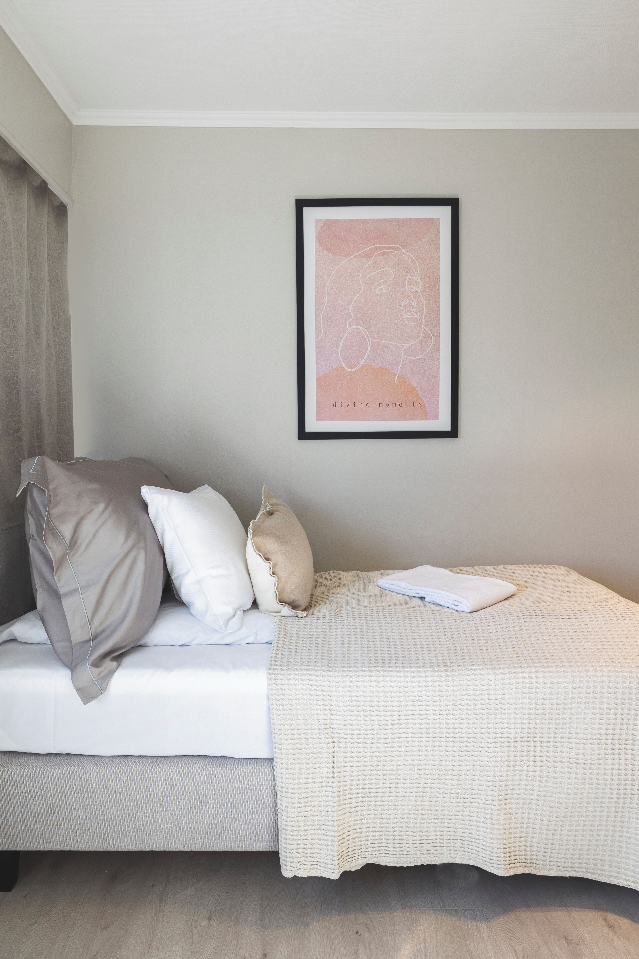 Ein ordentlich bezogenes Bett mit einer weiß-beigen Decke, zwei Kissen und einem gerahmten Bild an der Wand.