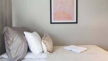 Ein ordentlich bezogenes Bett mit einer weiß-beigen Decke, zwei Kissen und einem gerahmten Bild an der Wand.