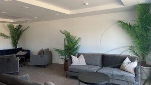 A modern living room with a grey sofa, a round coffee table, and two armchairs. There are several potted plants and a ceiling light fixture. - Victoria hotell Fredrikstad (Fredrikstad)