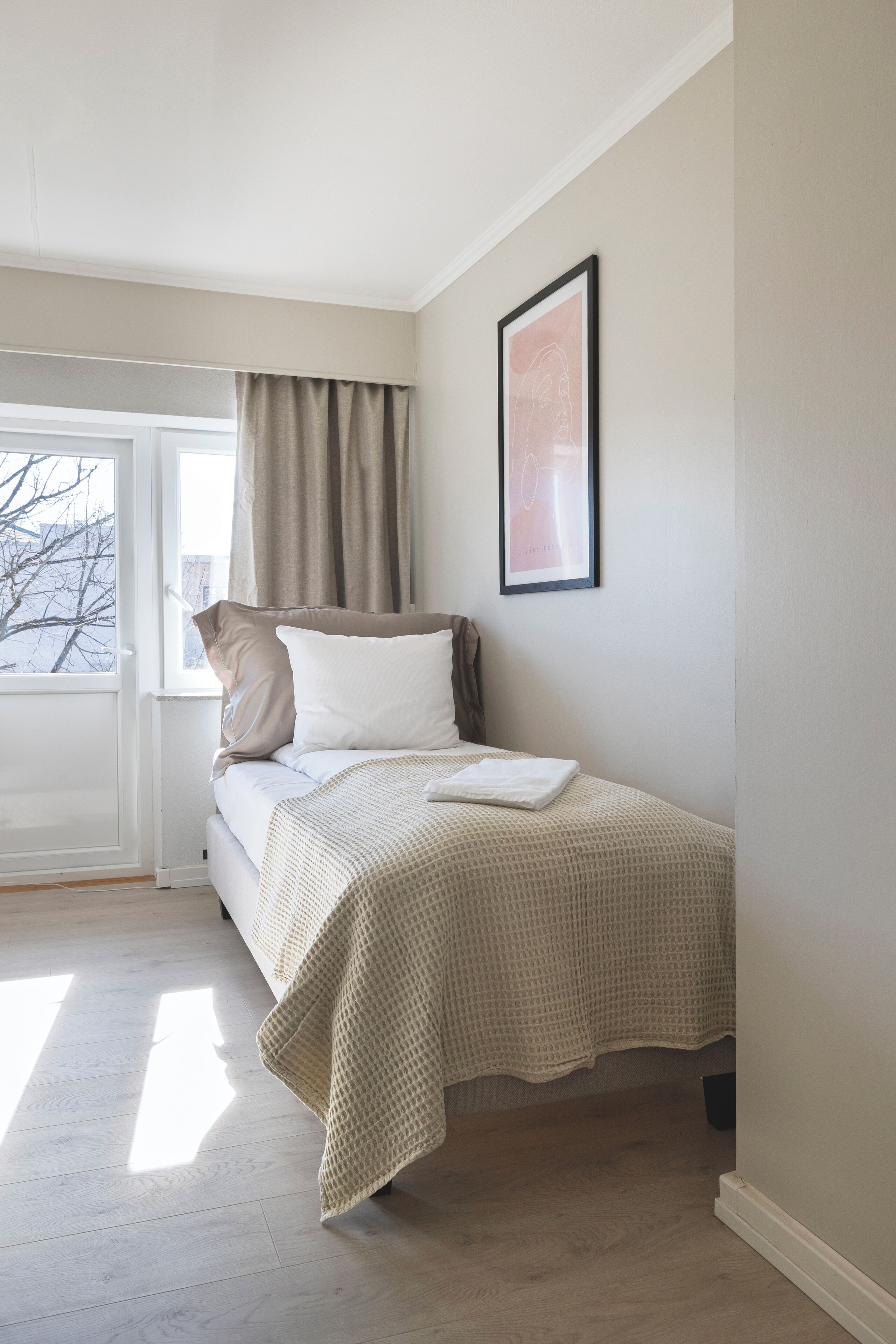 Un dormitorio ordenado con una cama, una ventana con cortinas y un cuadro en la pared.