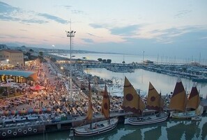 A marina with numerous sailboats docked, a bustling waterfront area with people and boats, and a distant bridge. - Beach house (Cattolica)