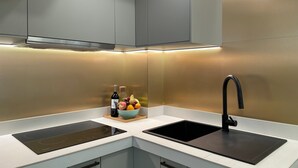 Eine moderne Küche mit zwei schwarzen Induktionskochfeldern, einem schwarzen Wasserhahn und einer Obst- und Weinschale auf der Arbeitsfläche.