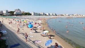 Ein Strand mit Sonnenschirmen, Personen und Gebäuden im Hintergrund.