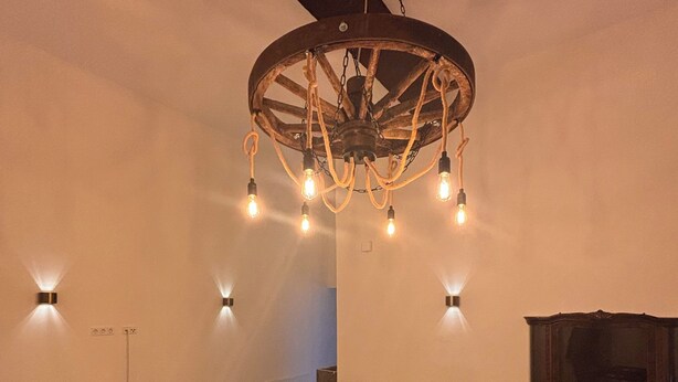 Una habitación amplia con una gran lámpara de madera, dos sillones tapizados, una mesita redonda y un mueble de madera oscura.
