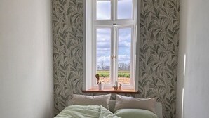 Una cama pequeña y ordenada en una habitación con ventana que da a un campo.
