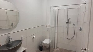 Un baño con un espejo redondo, un lavabo sobre encimera, un inodoro y una zona de ducha con mampara de vidrio.