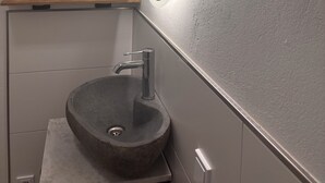 Un baño con un espejo redondo, un lavabo sobre encimera y un estante de madera encima.