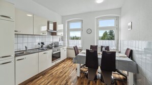 A modern kitchen with white cabinets, a wooden floor, and a dining area with a table and chairs. - Wupper Home II, top location Ideal for business people, fitters, families, 3 rooms (Wuppertal)