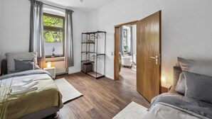 A modern bedroom with two beds, a wooden floor, a bedside table with a lamp, and a window with curtains. - Wupper Home II, top location Ideal for business people, fitters, families, 3 rooms (Wuppertal)