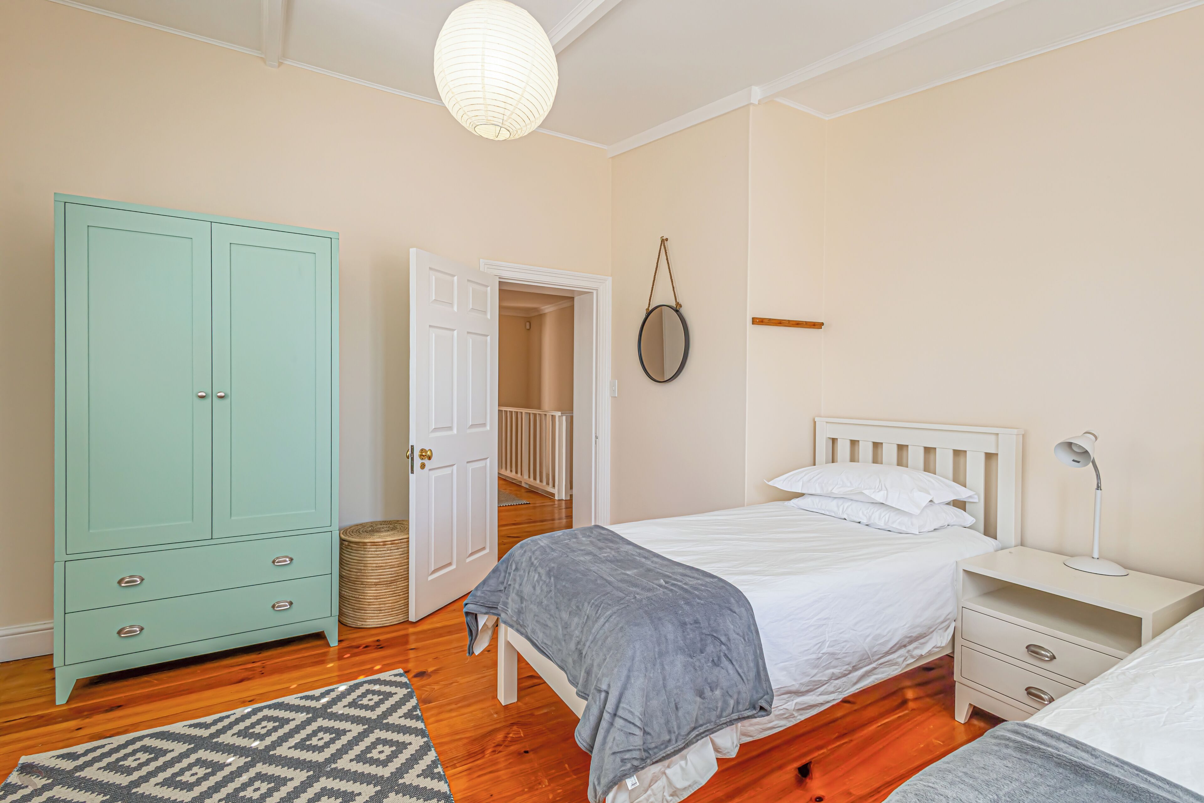 Quarto com cama, mesa de cabeceira, luminária, guarda-roupa e uma porta que dá para outro cômodo.