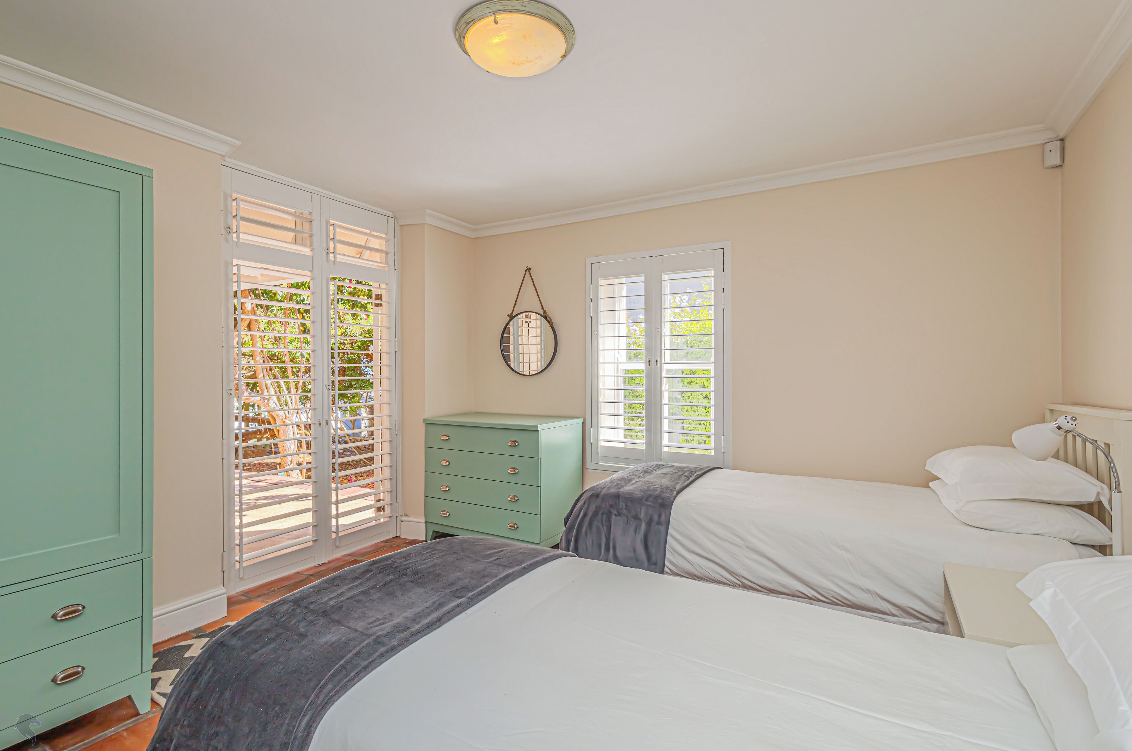 A bedroom with two beds, a green dresser, and a window with blinds.