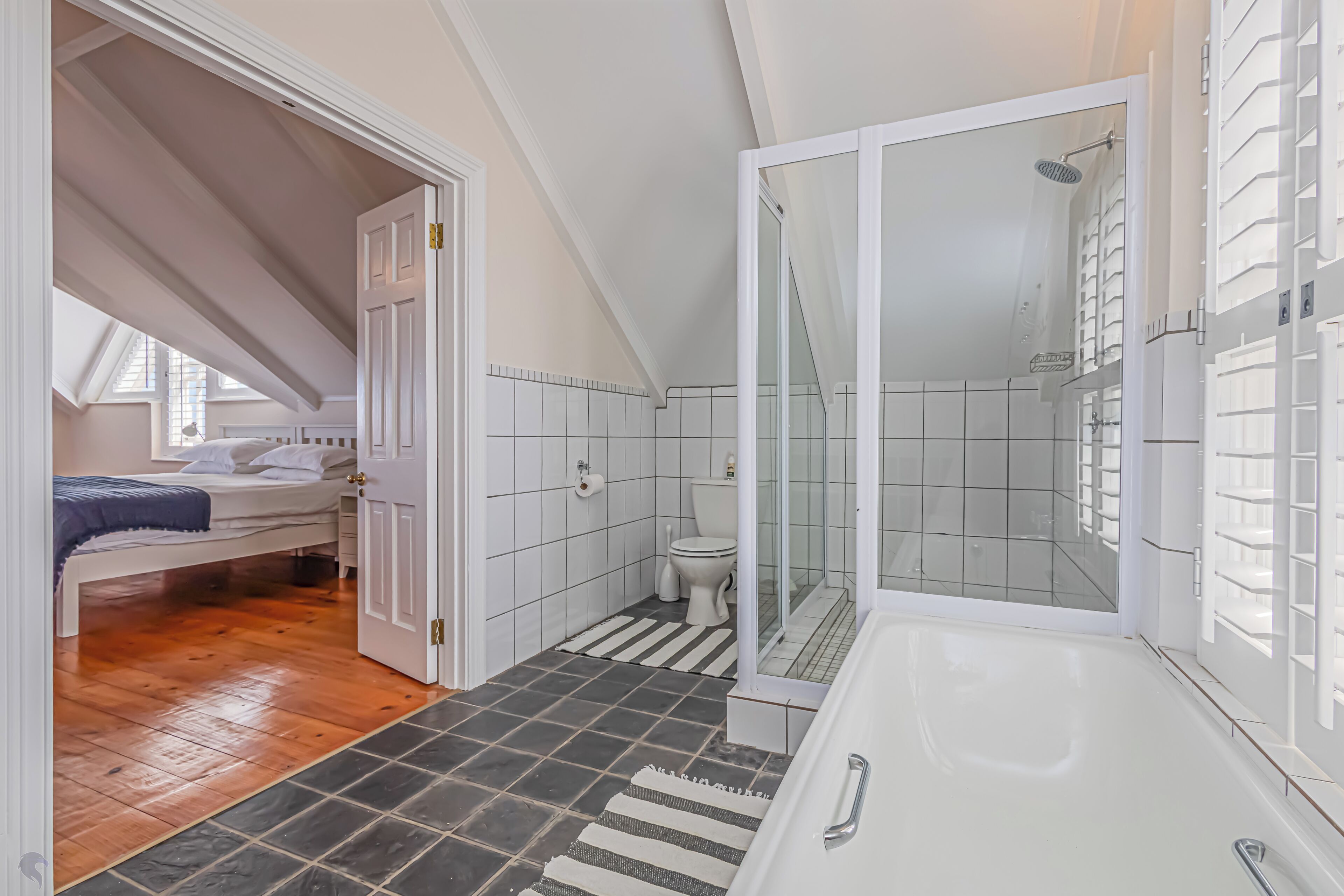 Une chambre avec un plafond en pente, une salle de bain avec une douche en verre, et de petits toilettes.