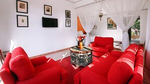 A room with red sofas, a television on the wall, and a decorative table with a vase. - Le Bled (Marrakech)