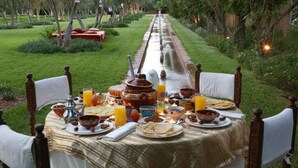 A dining table set outdoors with various dishes and drinks, surrounded by chairs. - Le Bled (Marrakech)