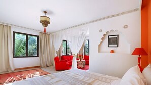 A hotel room with a large bed, a red sofa, a small table with a vase, and a red lamp. - Le Bled (Marrakech)