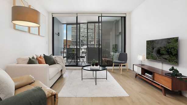 A modern living room with a sofa, coffee table, and TV. There is a sliding glass door leading to a balcony with outdoor furniture. - RARE FIND! Modern 2 Bdrm, 2 Bath, 1 Car in Central Sydney (City of Sydney)