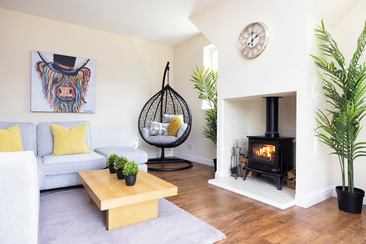 A living room with a sofa, a hanging chair, a wooden coffee table, a fireplace, and a painting on the wall.