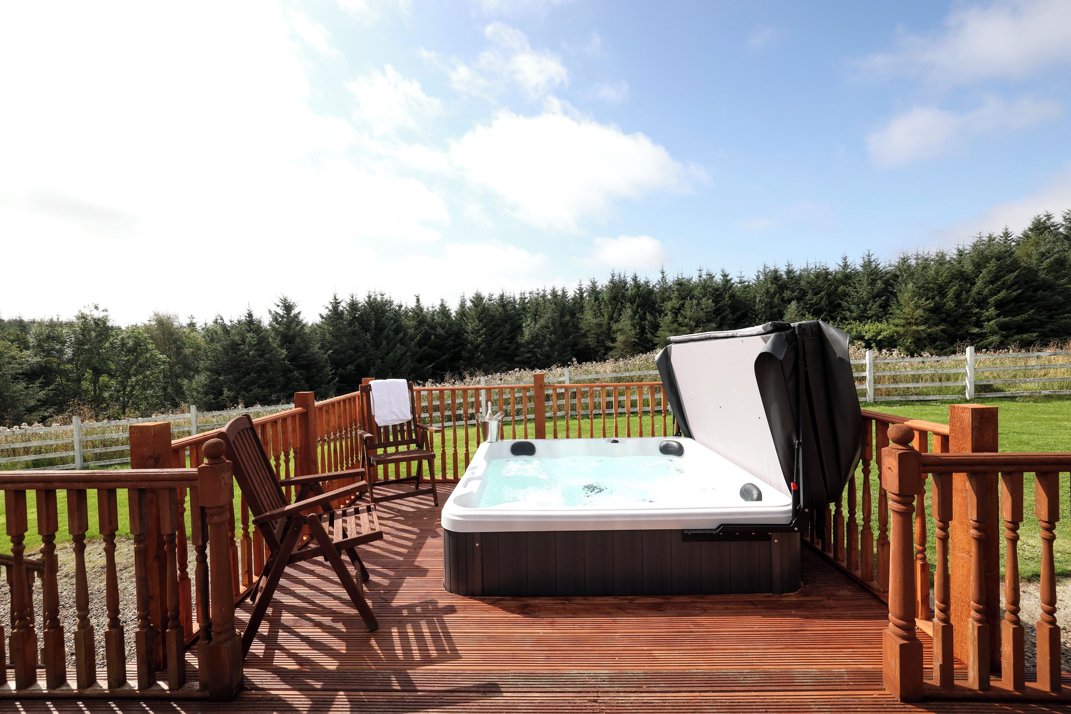 A hot tub on a wooden deck with a view of a forest.