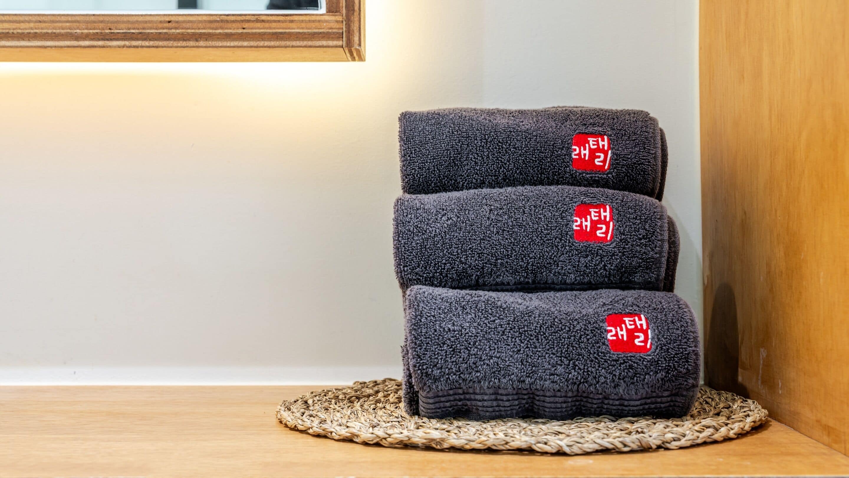Three folded towels with red labels on a woven mat.