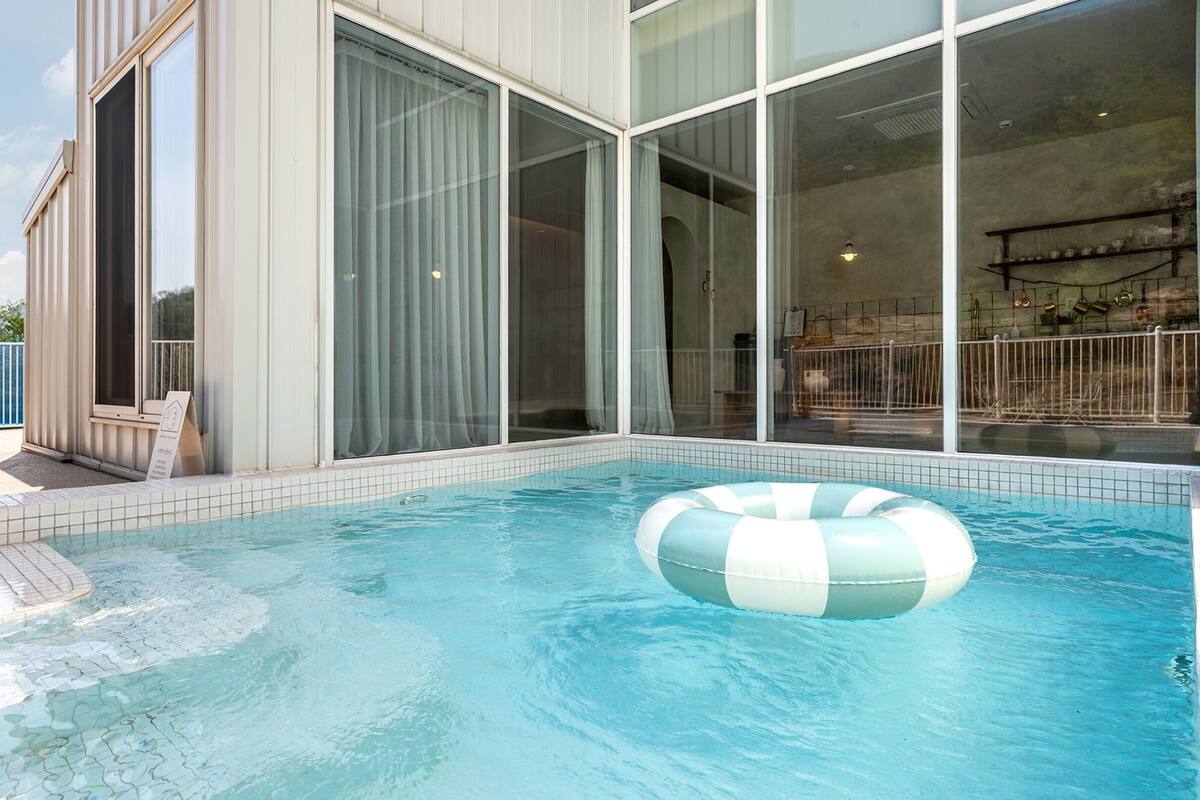 A swimming pool with a lounge chair and a large windowed room.